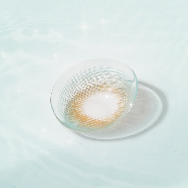 Aqua Playday contact lens with aqua and hazel design, displayed on a reflective surface for a natural eye enhancement.