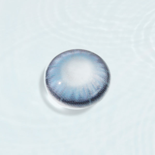 Pretty Blue Affair contact lens with intricate blue design, displayed on a reflective surface, ideal for enhancing eye color with a natural look.